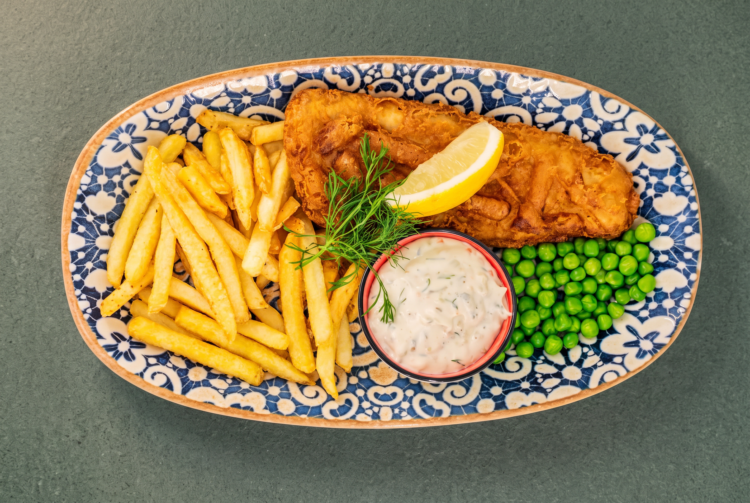 Fiskrätt med pommes, ärtor, citron och dill på blåmönstrat fat