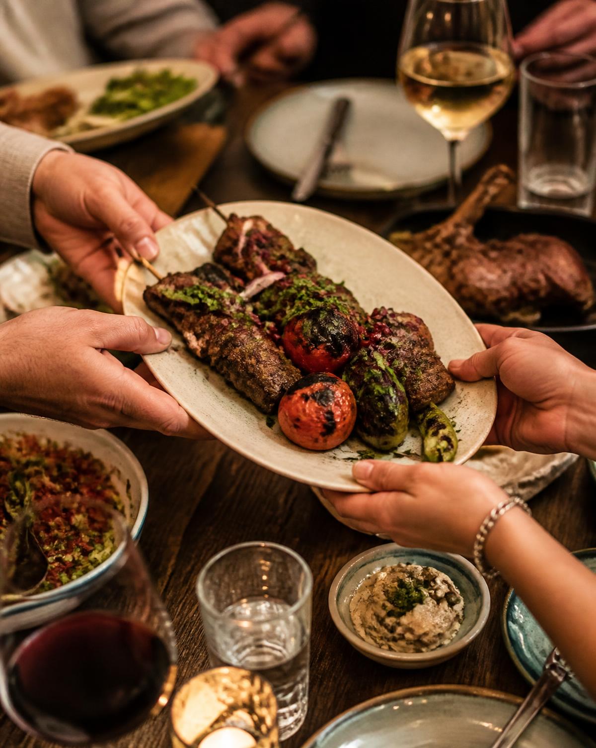 Händer som räcker över ett fat grillat vid middagsbordet